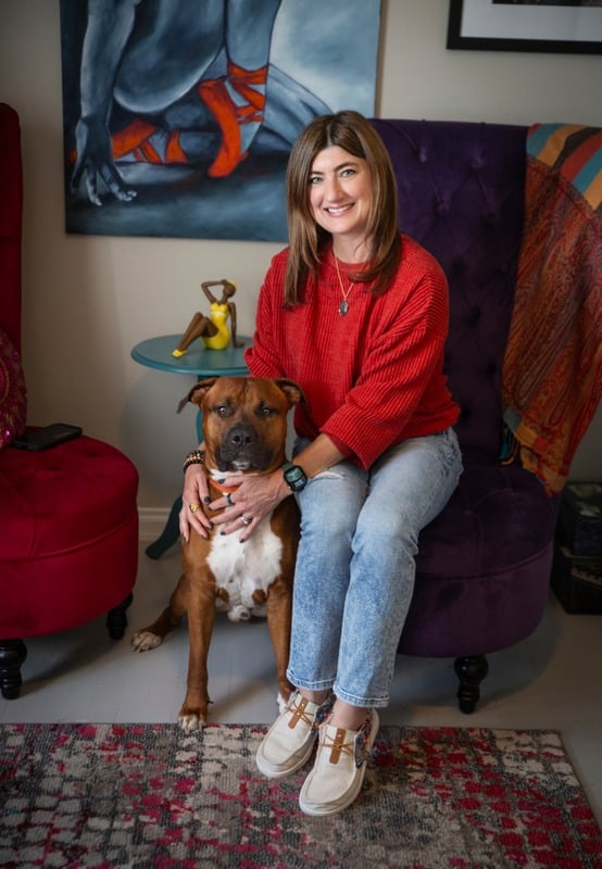 Lauren sitting with her dog in a warmly styled room.