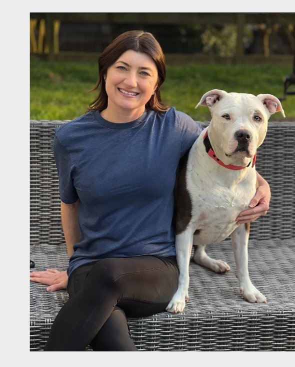 Lauren sitting outside on a patio couch with her white-and-brindle pit bull.